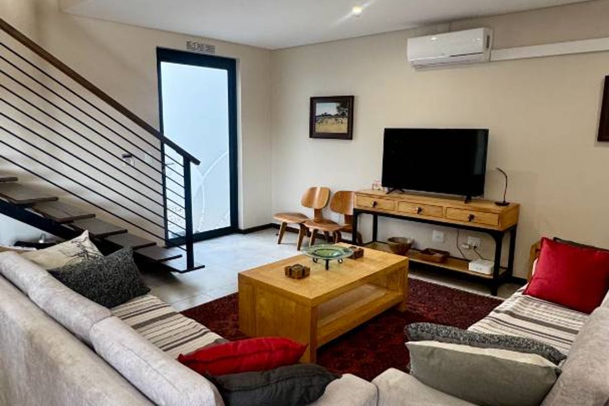 A well-lit living room featuring tiled flooring, a modern staircase with metal balustrades, and a wall-mounted split-system air conditioner.