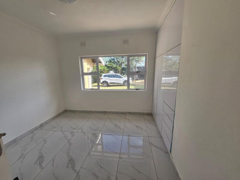 A bright, empty bedroom featuring modern marble-look floor tiles and sleek, floor-to-ceiling built-in cupboards.