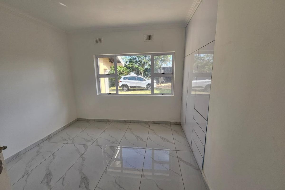 A bright, empty bedroom featuring modern marble-look floor tiles and sleek, floor-to-ceiling built-in cupboards.
