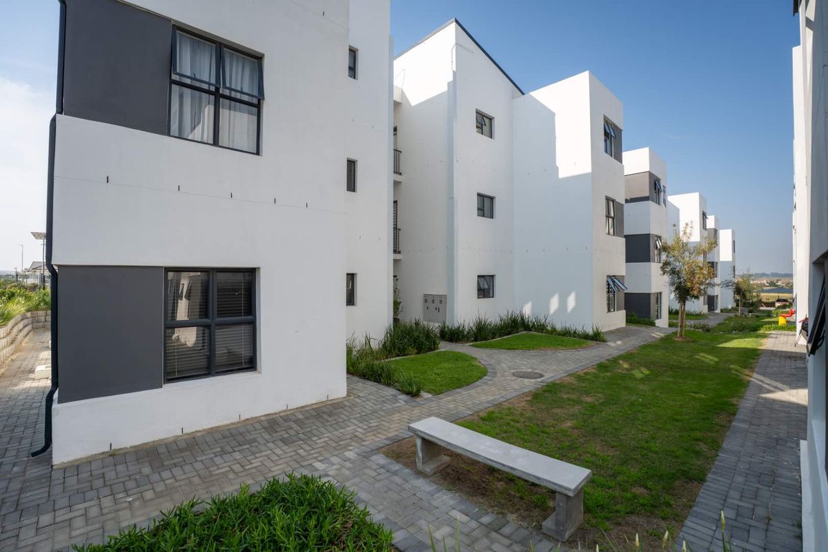 A well-maintained exterior view of a modern apartment complex featuring paved walkways, manicured lawns, and contemporary white building facades.
