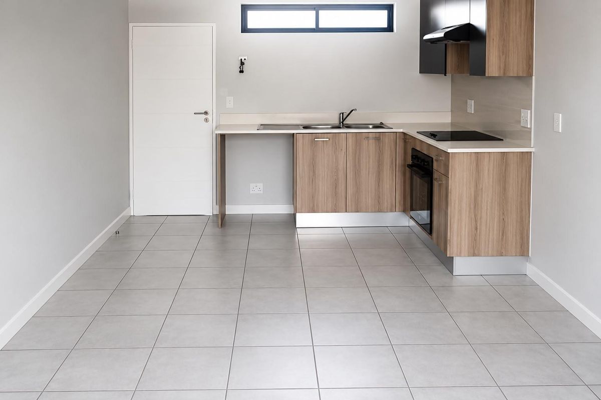 A clean, modern kitchen featuring light wood-finish cabinetry, integrated appliances, neutral tiled flooring, and a functional layout with ample counter space.