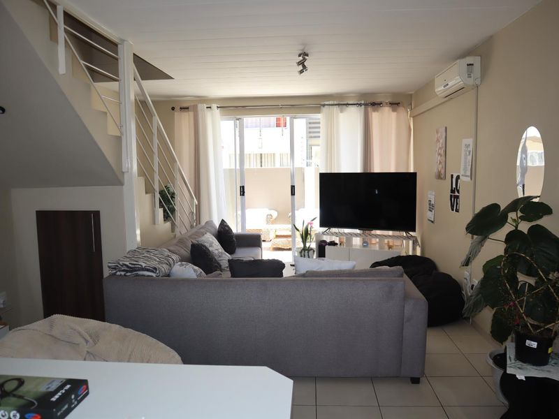 A comfortable living room featuring tiled flooring, a staircase, and a sliding glass door leading to an outdoor area, equipped with a wall-mounted air conditioner.