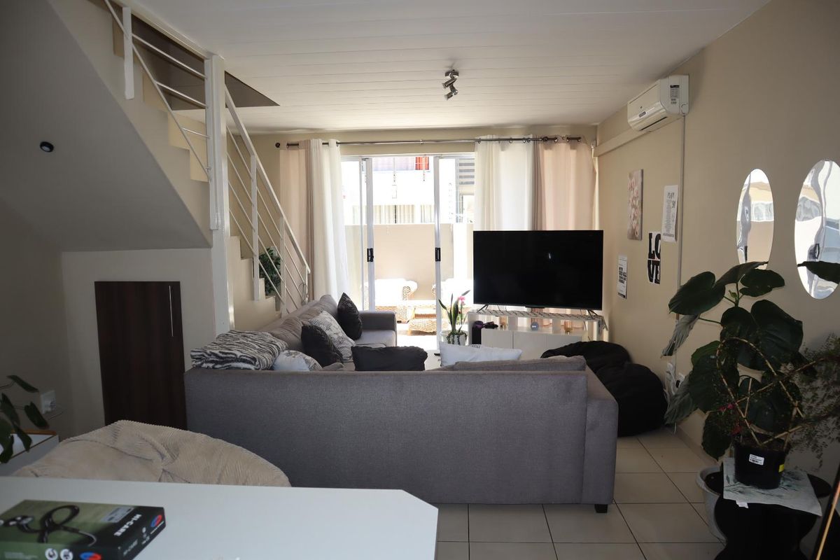 A comfortable living room featuring tiled flooring, a staircase, and a sliding glass door leading to an outdoor area, equipped with a wall-mounted air conditioner.
