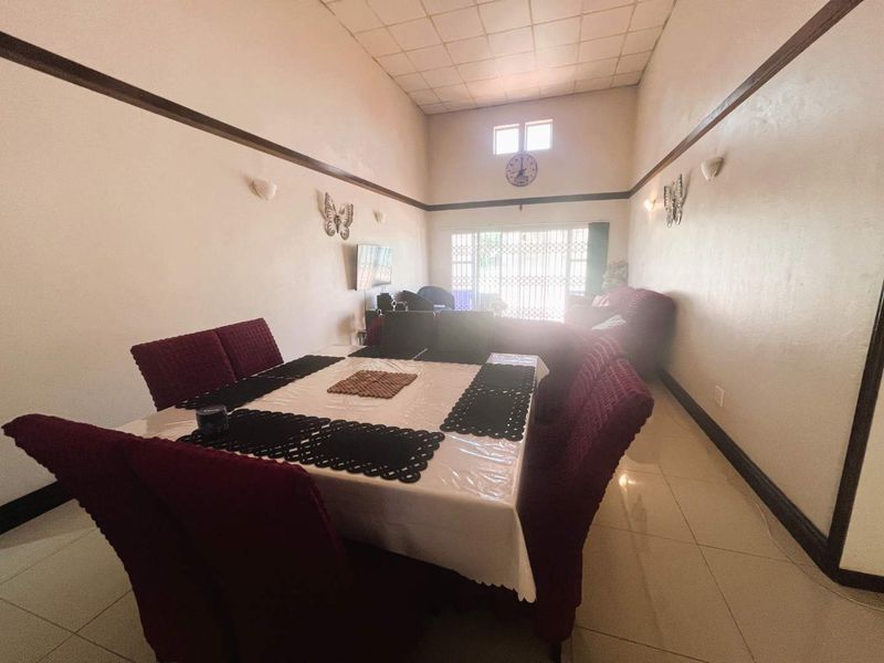Spacious open-plan living and dining area featuring high ceilings, tiled flooring, and large windows with security gates.