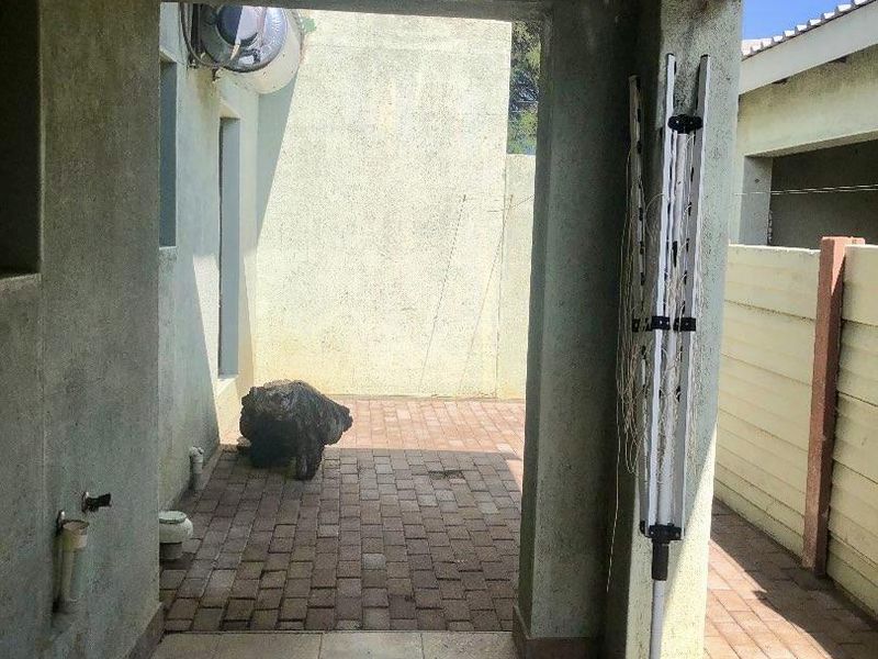 A covered outdoor patio area featuring paved flooring and exterior wall finishes, suitable for a small seating area or utility space.