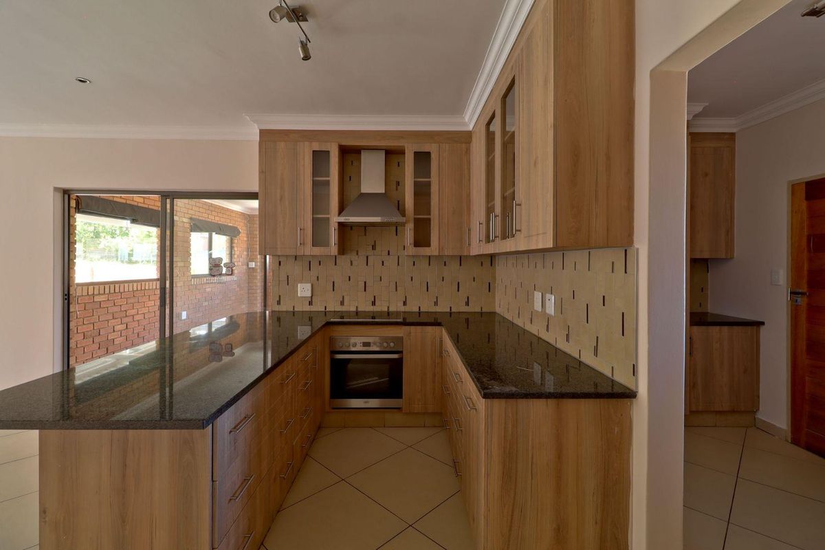 Modern kitchen featuring light wood cabinetry, dark granite countertops, built-in oven and hob, and a tiled backsplash, with direct access to the patio.