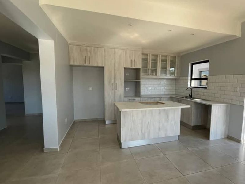 A modern, empty kitchen featuring light wood-look cabinetry, a central island, subway tile backsplash, and neutral floor tiles.