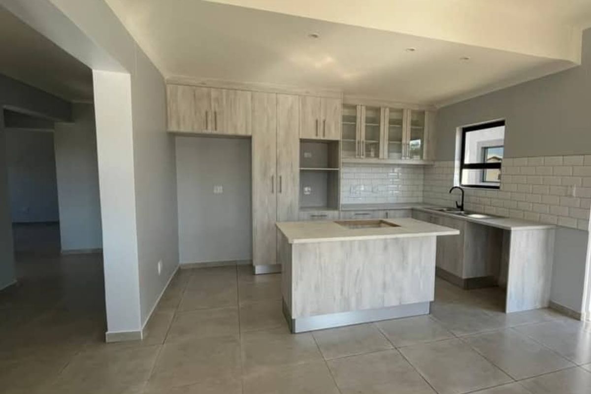 A modern, empty kitchen featuring light wood-look cabinetry, a central island, subway tile backsplash, and neutral floor tiles.