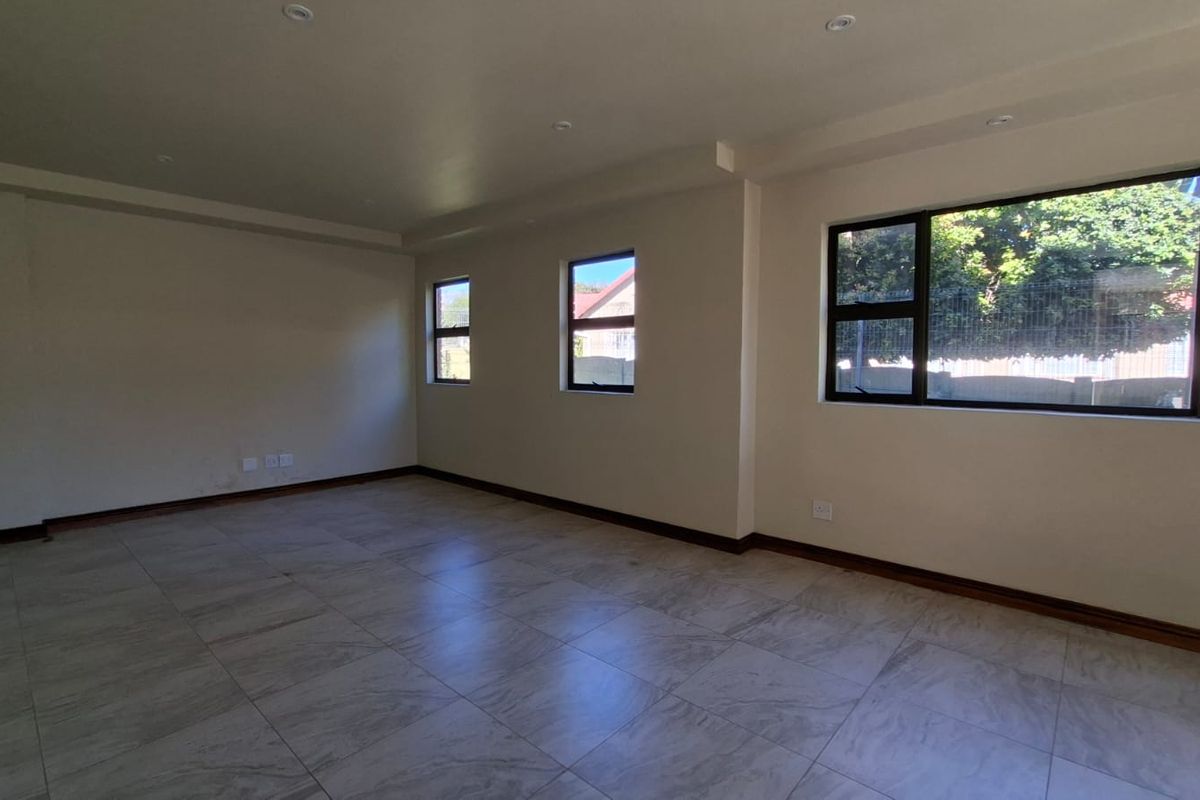 A spacious, empty living area featuring neutral tiled flooring, recessed ceiling lighting, and large windows that provide ample natural light.