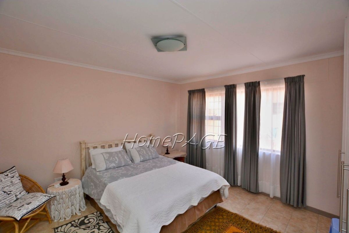 A well-lit bedroom featuring tiled flooring, neutral wall finishes, and large windows with curtain tracks.
