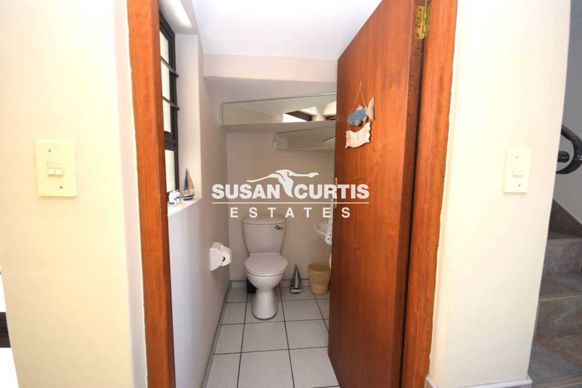 A compact guest bathroom featuring a toilet, wall-mounted basin, and tiled flooring, accessible via a wooden door.