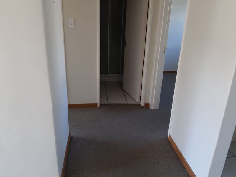 A neutral hallway with carpeted flooring leading to a bathroom with a shower enclosure.