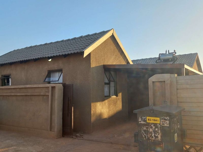 Front view of a single-story residential house featuring a tiled roof, solar geyser, and a private carport with boundary walling.