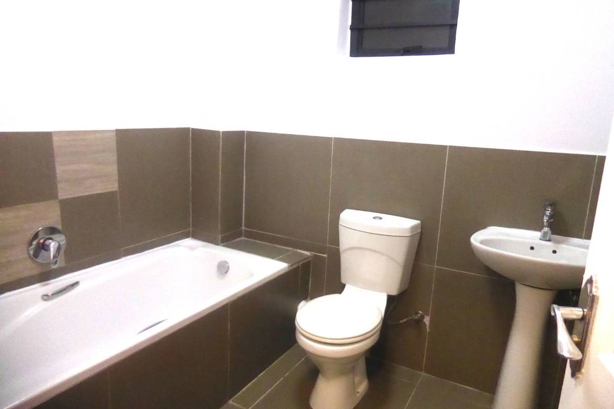 A clean, functional bathroom featuring a built-in bathtub, pedestal basin, and neutral wall tiling with a louver window for ventilation.