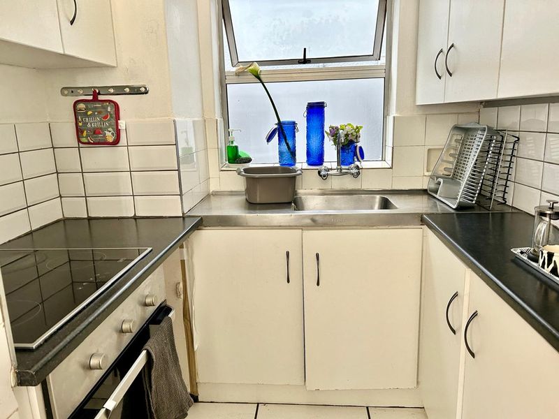 Compact kitchen featuring white cabinetry, dark laminate countertops, a built-in oven with electric hob, and a stainless steel sink with tiled splashback.