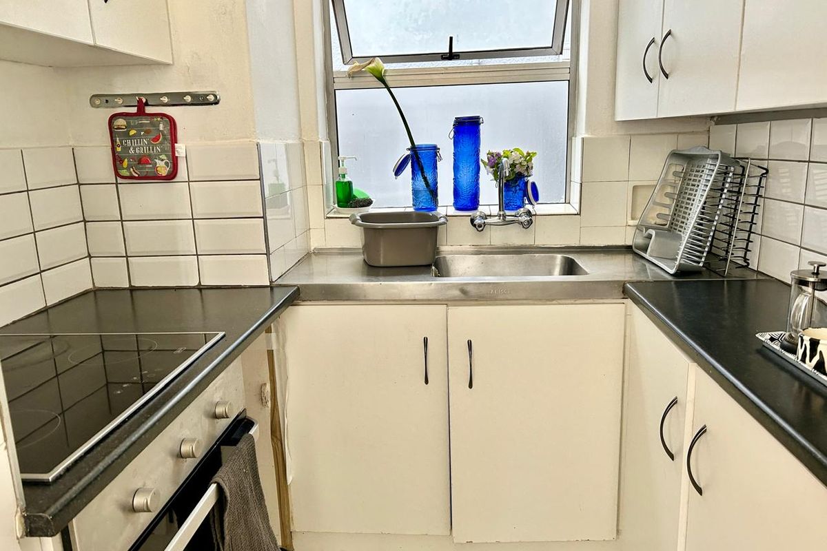 Compact kitchen featuring white cabinetry, dark laminate countertops, a built-in oven with electric hob, and a stainless steel sink with tiled splashback.