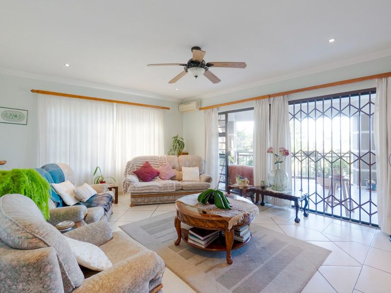 Spacious living room featuring tiled flooring, a ceiling fan, and large sliding glass doors with security gates leading to an outdoor patio area.