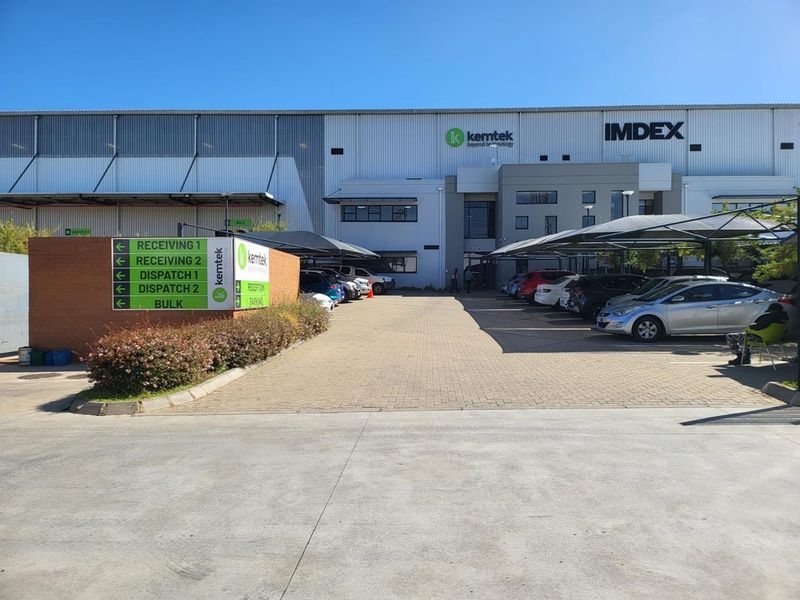 Industrial facility exterior featuring a paved parking area with shade cloth carports, signage, and clear access points for receiving and dispatch.