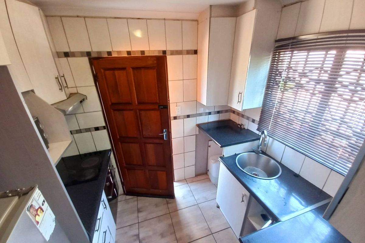 Compact kitchen featuring dark countertops, white cabinetry, tiled splashbacks, a built-in hob with extractor fan, and a stainless steel sink.