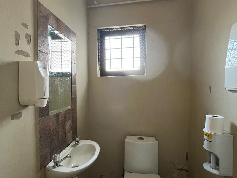 A compact bathroom featuring a wall-mounted basin and toilet, requiring cosmetic updates to the walls and flooring to improve its overall condition.