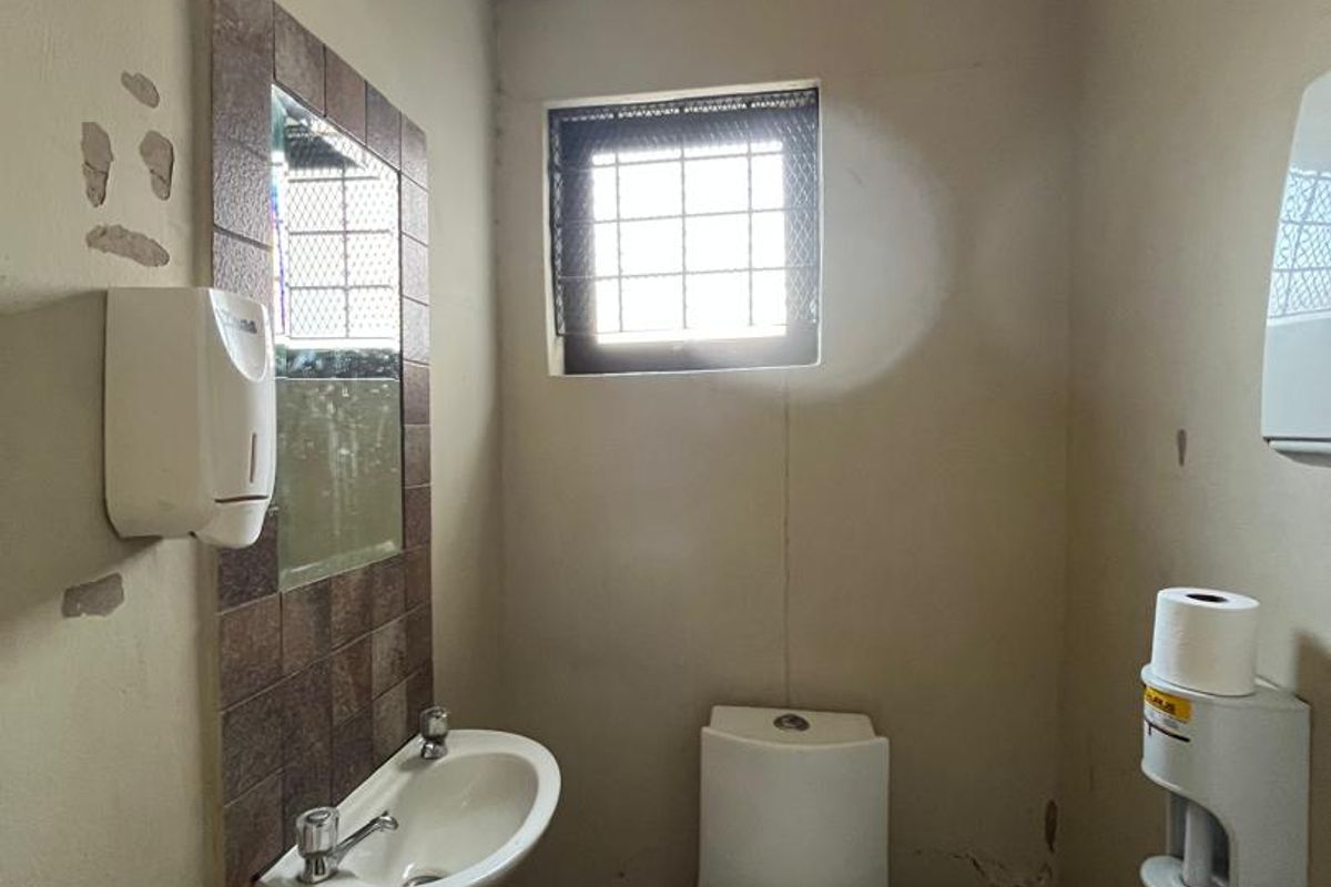 A compact bathroom featuring a wall-mounted basin and toilet, requiring cosmetic updates to the walls and flooring to improve its overall condition.