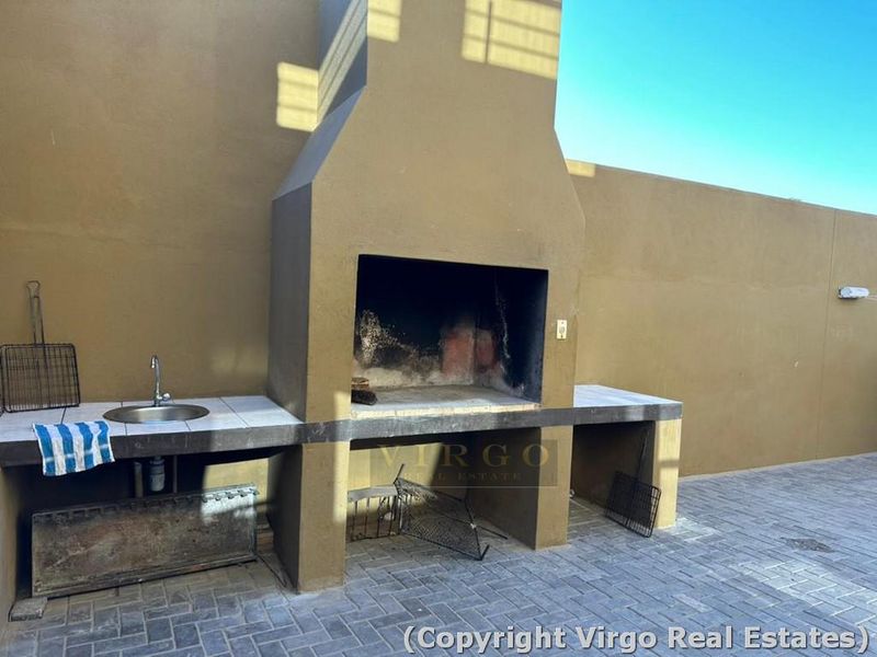 Outdoor patio area featuring a built-in braai, tiled prep counter with integrated sink, and paved flooring.