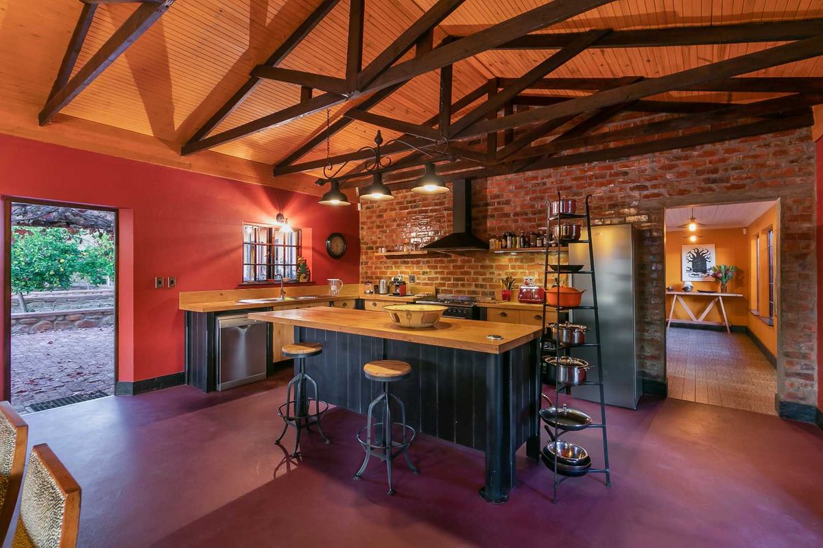 Spacious farmhouse kitchen featuring exposed timber trusses, brick feature wall, wooden countertops, and a central island, creating a warm and rustic atmosphere.