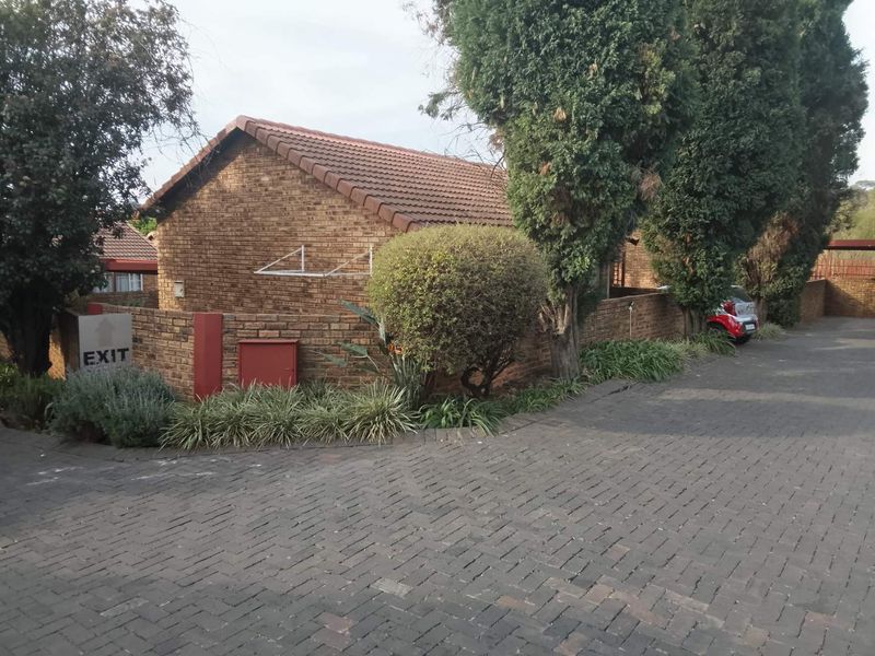 Exterior view of a face brick townhouse featuring a tiled roof, paved driveway, and established garden surroundings.