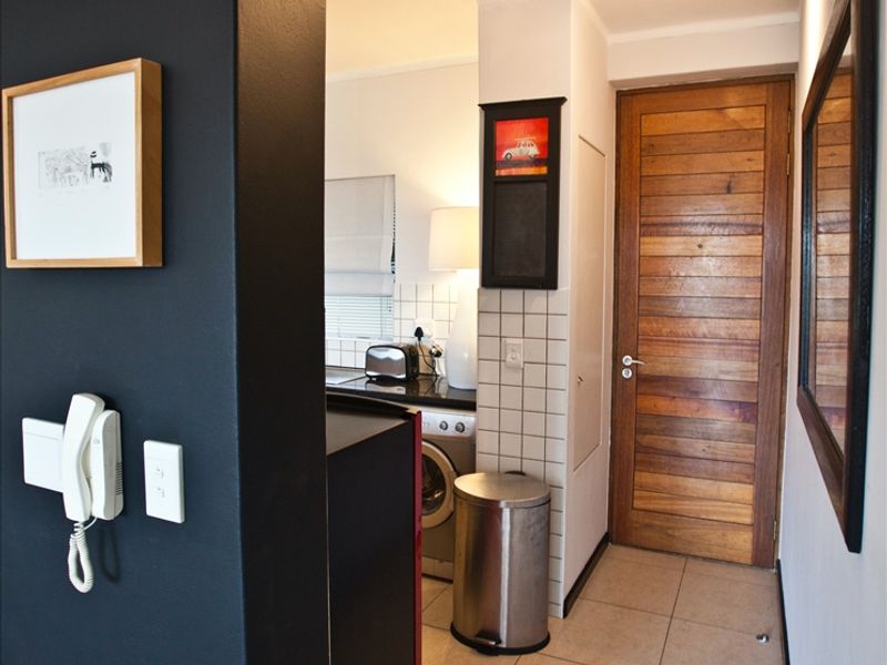 A functional hallway featuring tiled flooring, a solid timber door, and an integrated intercom system, providing access to the adjacent kitchen area.