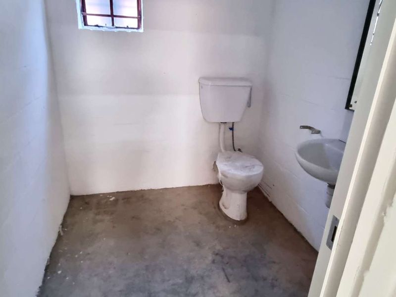 A basic industrial-style bathroom featuring a toilet, wall-mounted basin, and security-barred window, requiring significant cosmetic updates and finishing.