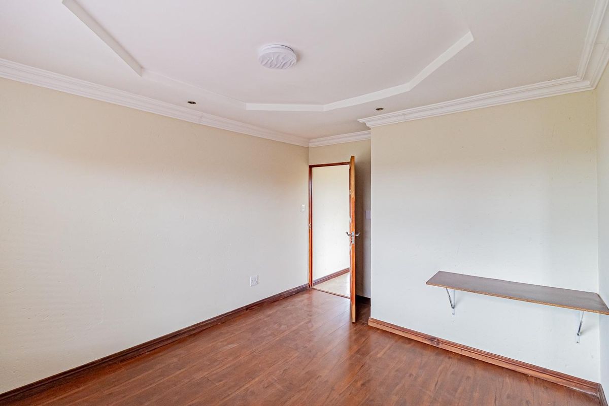 A vacant bedroom featuring laminate wood flooring, a decorative tray ceiling with recessed lighting, and a wall-mounted shelf.