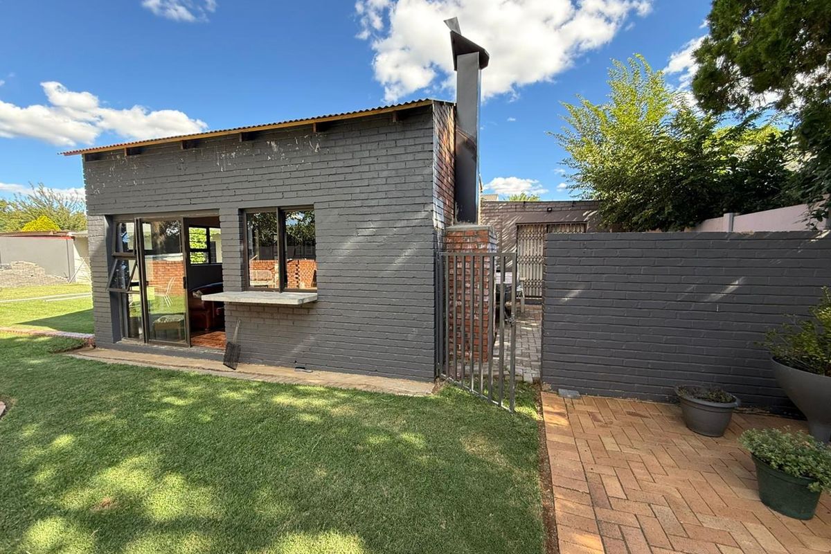 Rear view of a detached brick outbuilding featuring a built-in outdoor fireplace, sliding glass doors, and a paved patio area in the garden.