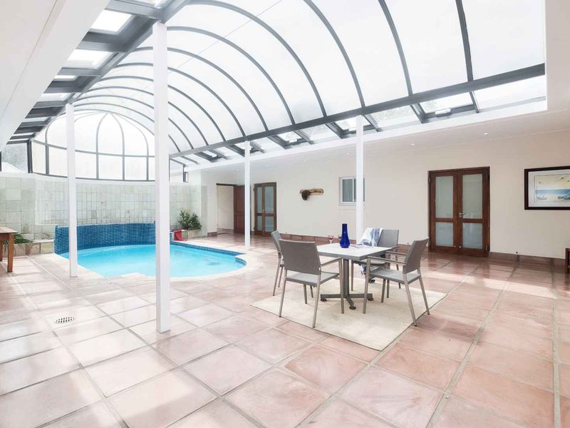 An indoor swimming pool area featuring a large arched glass roof, tiled flooring, and a spacious entertainment space.