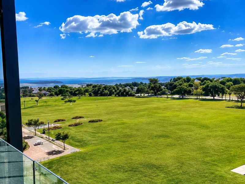 Elevated view overlooking a large green parkland area with distant water views, framed by a modern glass balcony balustrade.