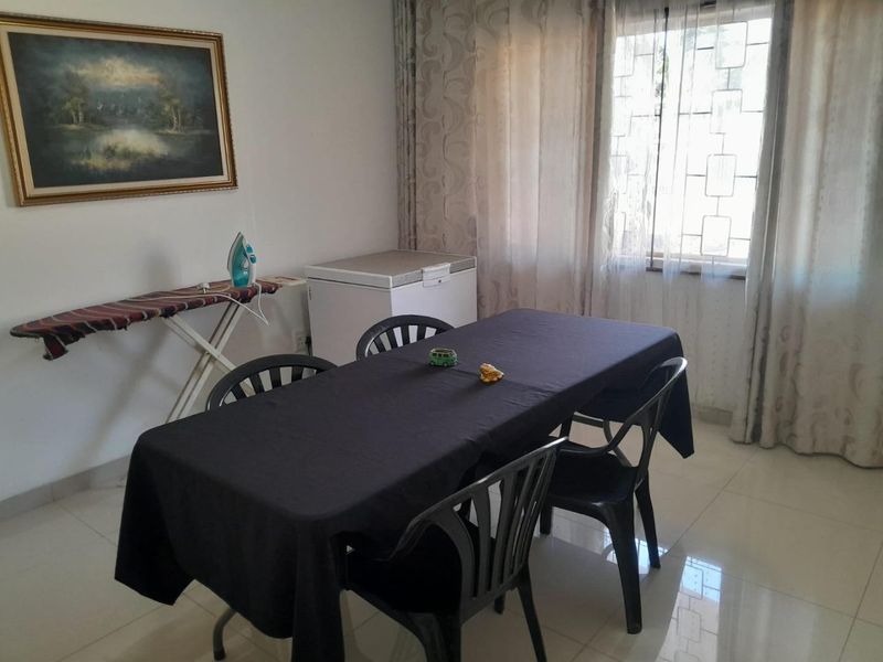 A functional dining area featuring tiled flooring and a window with security bars, providing a simple and practical space for meals.
