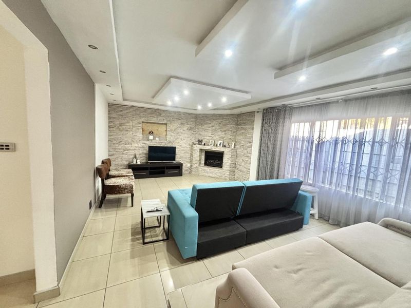 Spacious living room featuring a stone-clad feature wall with a built-in fireplace, recessed ceiling lighting, and large windows with security gates.