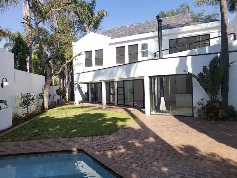 Rear view of a two-story cluster home featuring a swimming pool, brick-paved patio, covered entertainment area, and a balcony.