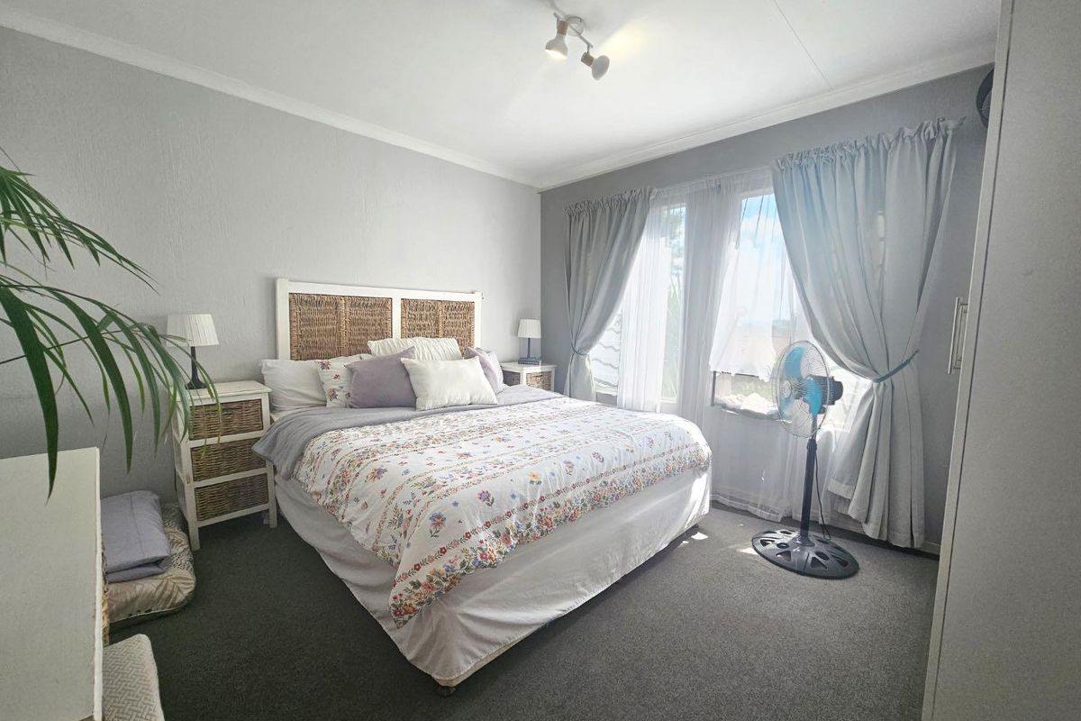 A well-lit bedroom featuring neutral wall tones, carpeted flooring, and large windows with curtains, providing a comfortable and functional living space.