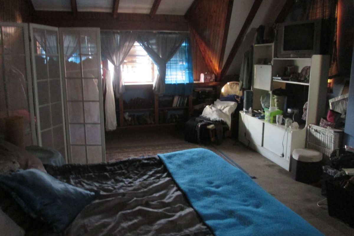 Attic-style bedroom featuring exposed timber ceiling beams and wood-paneled walls, offering a cozy, rustic atmosphere with integrated storage shelving.