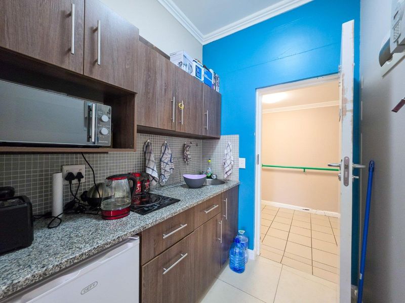 Compact kitchen featuring wood-look cabinetry, granite-style countertops, mosaic splashback, and built-in microwave, leading into a tiled hallway.