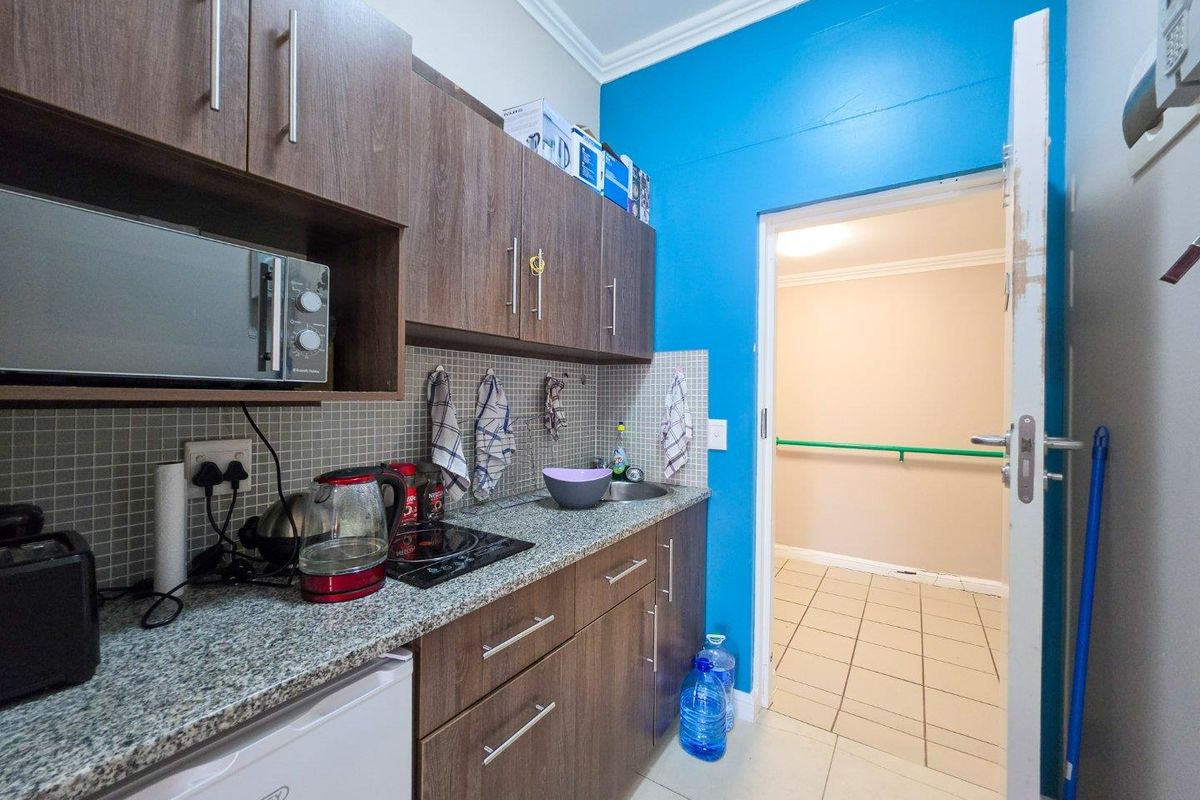 Compact kitchen featuring wood-look cabinetry, granite-style countertops, mosaic splashback, and built-in microwave, leading into a tiled hallway.
