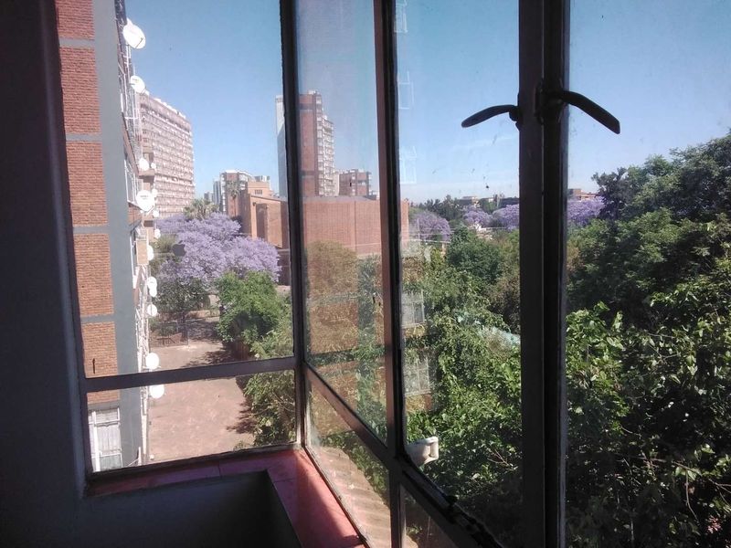 A view from an apartment window overlooking a leafy urban neighborhood with mature trees and surrounding residential buildings.