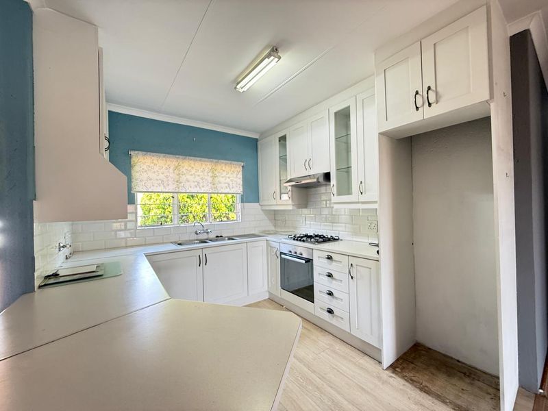 A functional kitchen featuring white cabinetry, subway tile backsplash, built-in oven, gas hob, and a dedicated fridge alcove with laminate flooring.