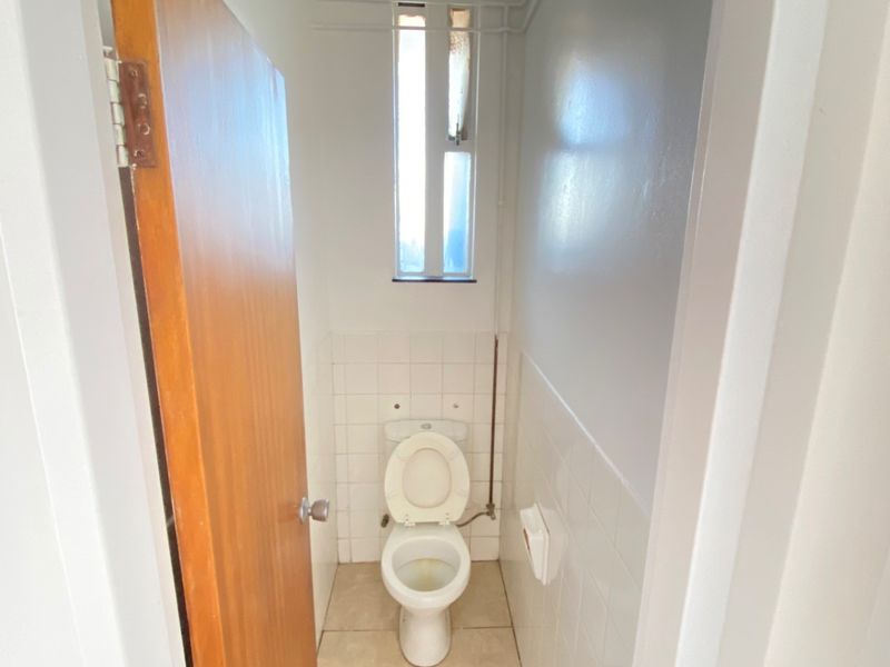 A compact, functional bathroom featuring a standard toilet, tiled wall accents, and a vertical window for natural light.