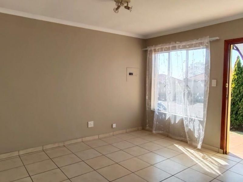 An empty, neutrally painted living room featuring tiled flooring, cove cornicing, and direct access to the exterior through a timber-framed door.