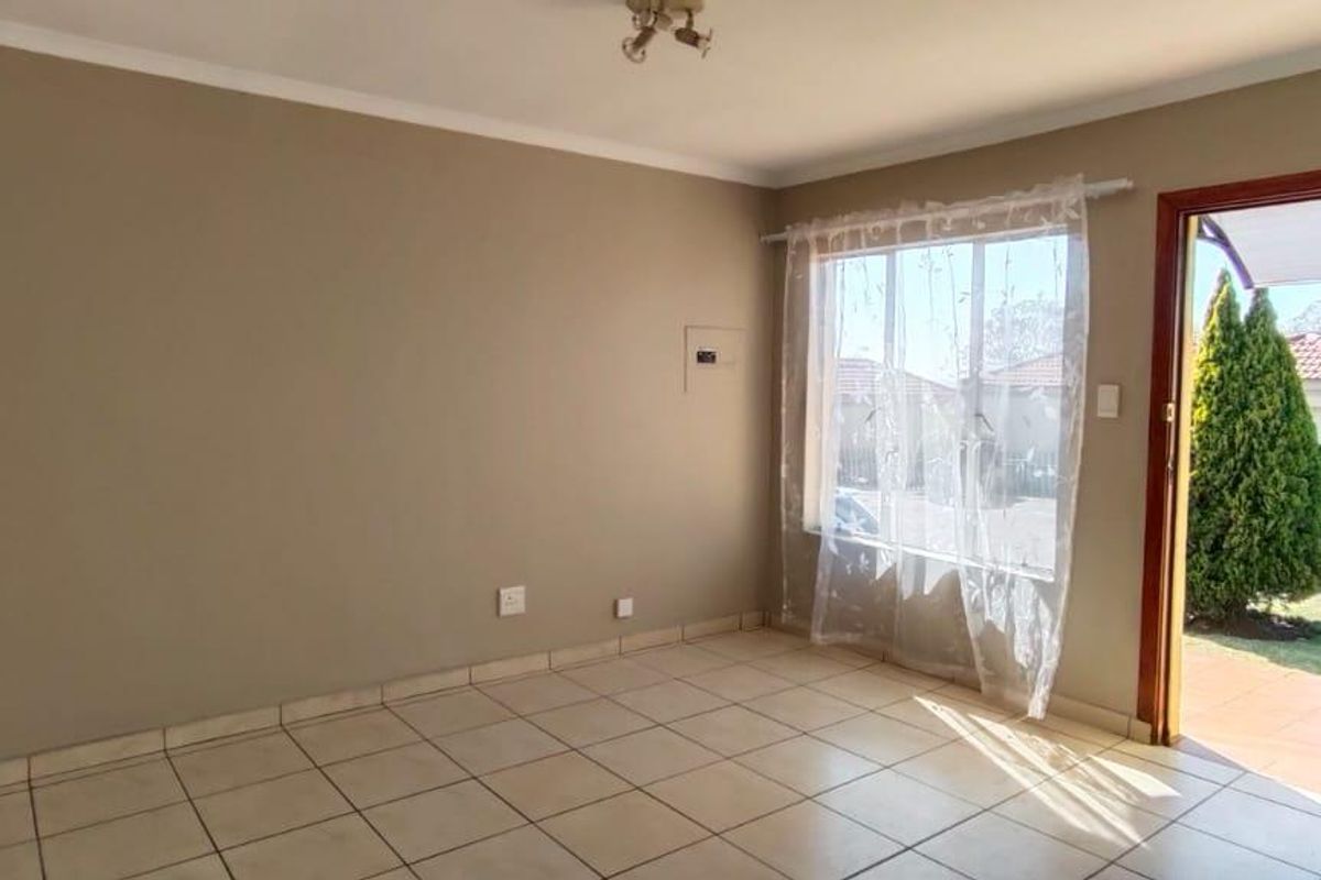 An empty, neutrally painted living room featuring tiled flooring, cove cornicing, and direct access to the exterior through a timber-framed door.