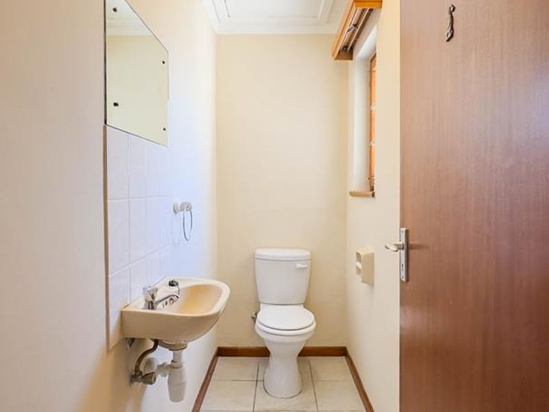 A compact guest bathroom featuring a wall-mounted basin, toilet, and tiled flooring, presenting a functional space ready for modernization.