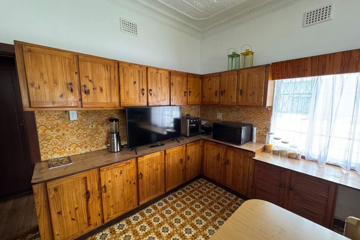 A dated kitchen featuring traditional timber cabinetry, patterned tile flooring, and decorative pressed metal ceiling details.
