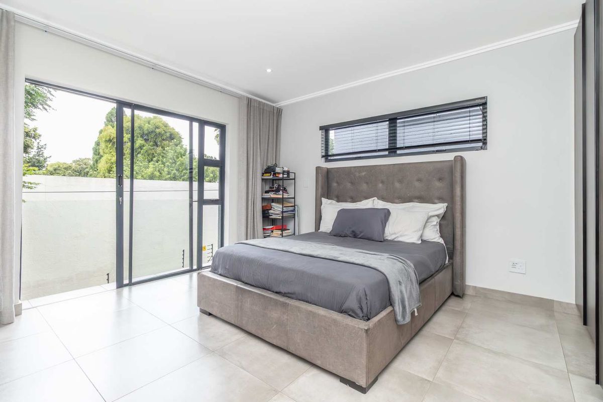 A bright, modern bedroom featuring large sliding glass doors that open to a private outdoor area, tiled flooring, and sleek window blinds.