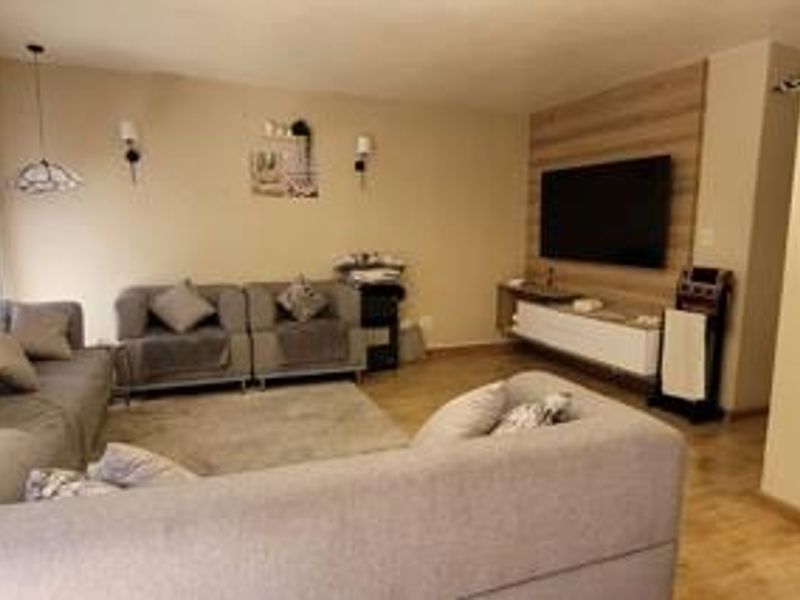 A comfortable living room featuring laminate flooring, a wood-look feature wall with a mounted media console, and wall-mounted lighting fixtures.